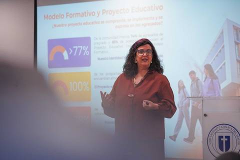 Una mujer presenta un proyecto educativo frente a una audiencia en una sala de clases.