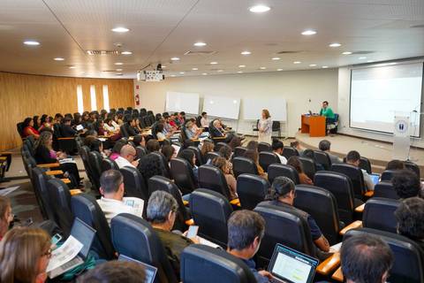 Una clase en un aula con muchos estudiantes atentos y un profesor al frente.