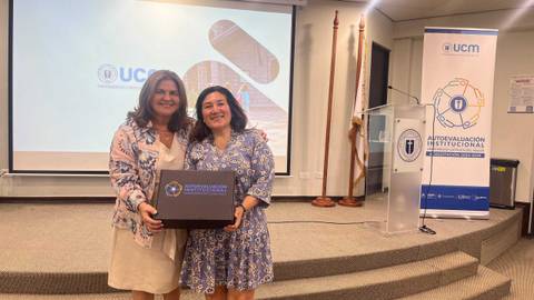 Dos mujeres posan juntas con una caja en un evento institucional en la UCM.