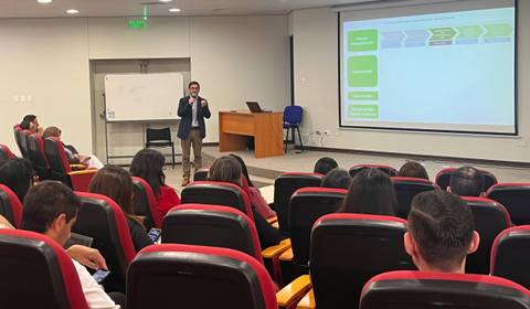 Una charla educativa en un auditorio con un expositor y público atento.