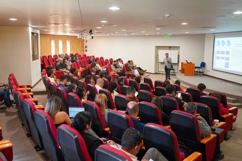 Una charla en un auditorio lleno de gente, con un expositor presentando en la pantalla.