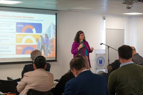 Una mujer presenta datos sobre un proyecto educativo frente a una audiencia en una sala de conferencias.