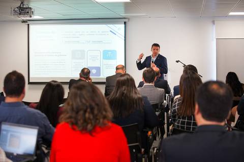 Un expositor presenta información a un grupo de asistentes en una sala de conferencias.