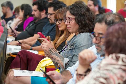 Un grupo de personas sentadas en un auditorio, mirando sus celulares y participando en una actividad.