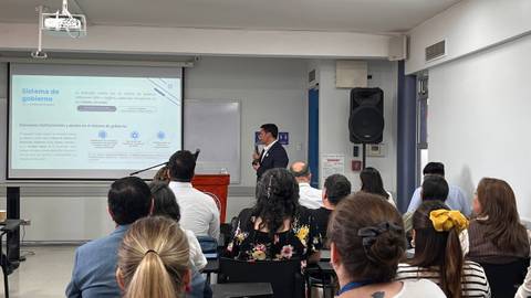 Un expositor presenta un tema sobre sistemas de gobierno ante un grupo de personas en un aula.