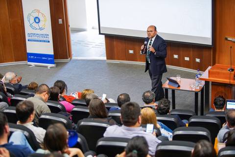 Un conferencista expone frente a un auditorio lleno durante un evento institucional.