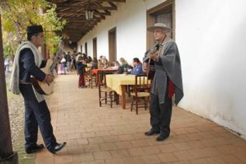 Dos músicos interpretan canciones en un ambiente al aire libre, rodeados de mesas y sillas.