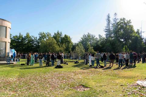 Un grupo grande de personas se reúne en un parque bajo un cielo despejado.