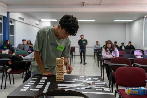 Un cabro jugándose una partida de Jenga en una sala de clases con compañeros de fondo.