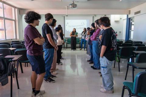 Un grupo de estudiantes escucha atentamente a una persona que está frente a ellos en un aula.