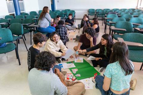 Un grupo de jóvenes se reúne en el suelo de una sala para realizar actividades creativas y colaborativas.