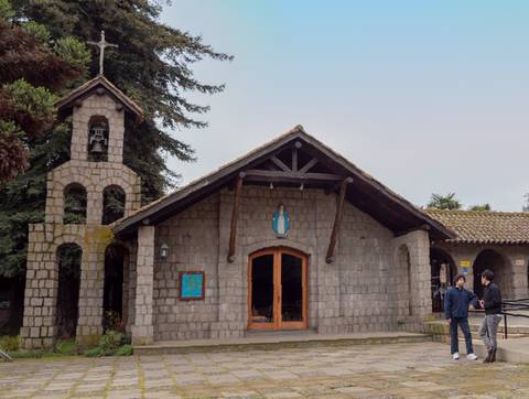 Una iglesia de piedra con una torre y dos personas conversando en su entrada.