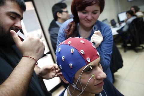 Un hombre con un casco de electroencefalografía es preparado por un grupo de personas en un entorno de laboratorio.