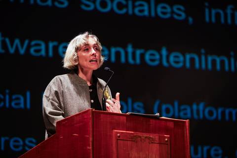Una mujer está exponiendo en un escenario frente a un auditorio.