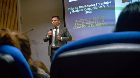 Un expositor presenta un taller sobre habilidades parentales ante una audiencia en un auditorio.