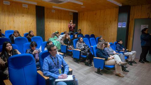 Un grupo de personas sentadas en un aula con asientos azules, atentos a una presentación.