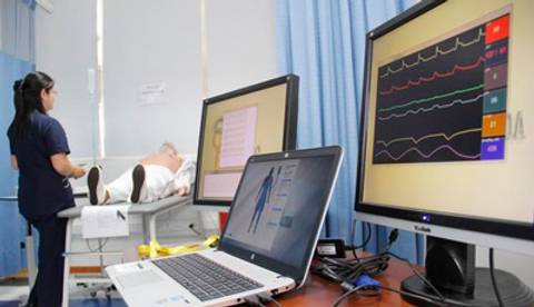 Una enfermera atiende a un paciente en una sala de consulta médica mientras se muestran gráficos en pantallas de computadora.