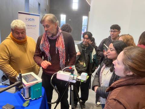 Un grupo de estudiantes y profesores discutiendo sobre un aparato tecnológico en una feria científica.