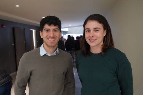 Dos amigos posando sonrientes en un pasillo.