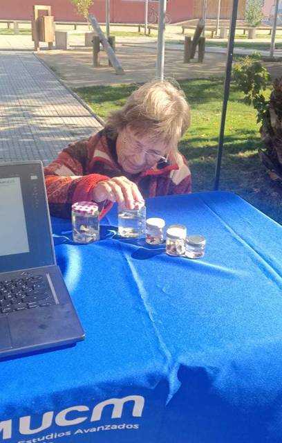 Una mujer está observando frascos con líquido sobre una mesa al aire libre.