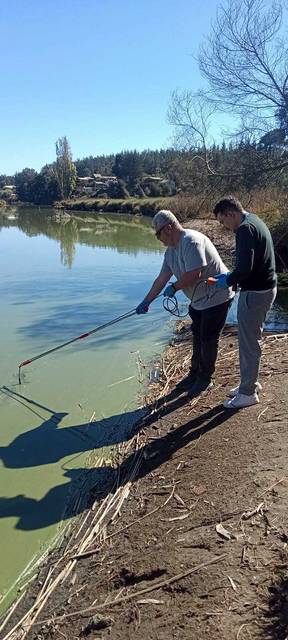 Dos personas están muestreadando agua en un río en un día soleado.