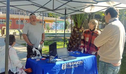 Un grupo de personas conversando en un stand al aire libre con un microscopio y computadora.