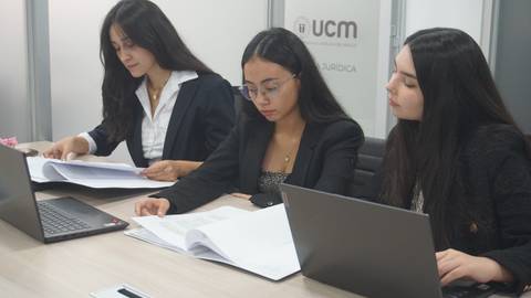 Tres mujeres profesionales revisando documentos en una oficina moderna.