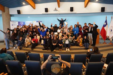 Un grupo grande de personas reunidas en una sala, celebrando y mostrando signos de alegría en un evento en Chile.