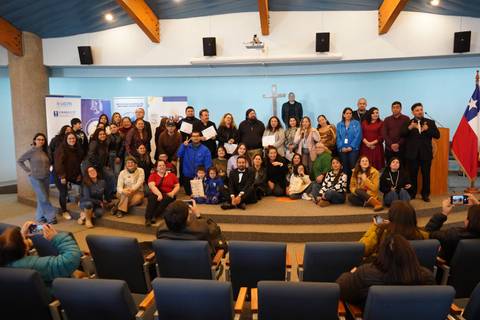 Un grupo grande de personas posando juntas en un evento en un salón con banderas chilenas.