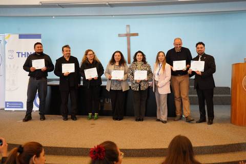 Un grupo de personas sonrientes sostiene certificados en una ceremonia en un auditorio.
