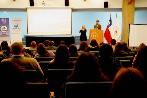 Una actividad académica en un auditorio con un presentador y una intérprete de lengua de señas.