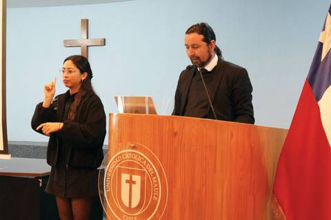 Un hombre presenta mientras una mujer se comunica en lengua de señas en un evento en la universidad.