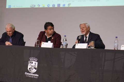 Un panel de discusión donde tres hombres comparten en una mesa frente a un público.