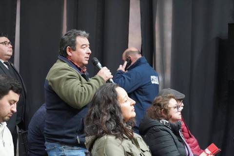Un grupo de personas asiste a un evento donde se escucha a un hombre hablar con un micrófono.