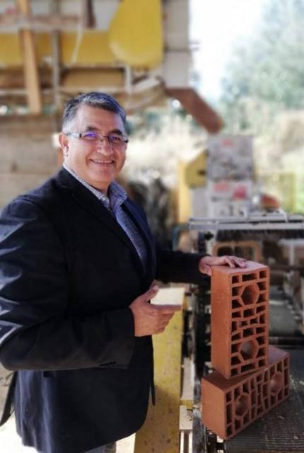 Un hombre sonriente muestra un ladrillo en una fábrica de construcción.