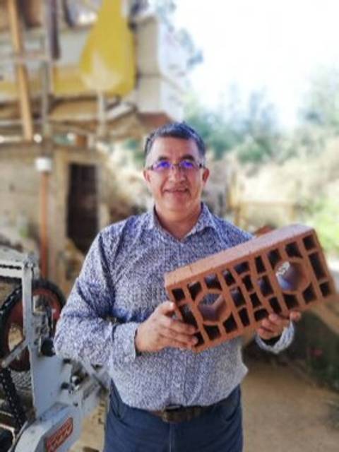 Un hombre sonriente sostiene un ladrillo en un entorno rural.