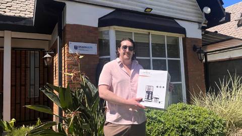 Un cabro posando frente a su casa con un regalo en las manos.