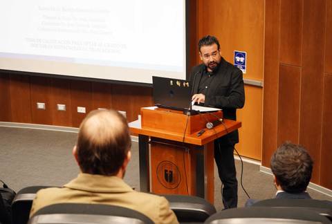 Un hombre está presentando en un auditorio, explicando un tema frente a un público atento.