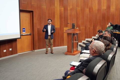 Un expositor presenta frente a un público atento en una sala de conferencias.