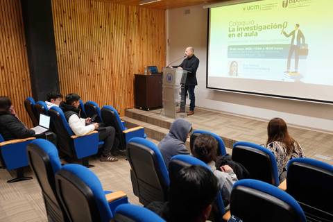 En un coloquio sobre investigación en el aula, un expositor se prepara para presentar ante un público atento.