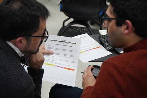 Dos personas conversando sobre un documento relacionado con metodologías de investigación.