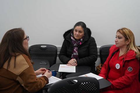 Tres mujeres se encuentran conversando en una reunión en un entorno cerrado.