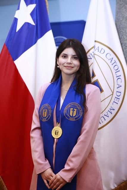 Una estudiante chilena vistiendo una chaqueta rosa con medalla y banda en un evento solemne, junto a las banderas de Chile y la universidad.