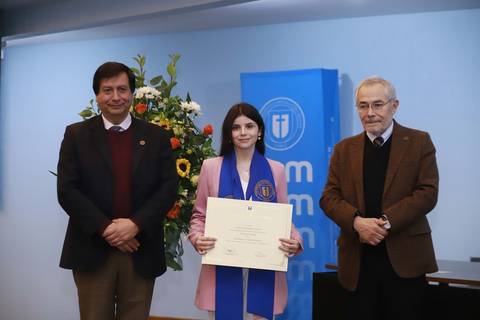 Una joven sonriente sostiene su diploma mientras está rodeada de dos hombres en un acto académico.