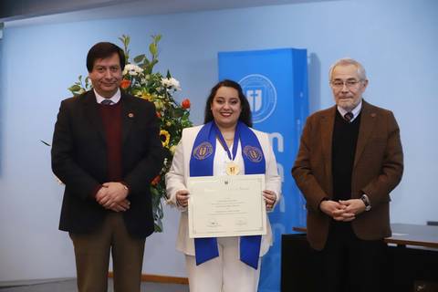 Una mujer con traje blanco sonríe mientras sostiene un diploma en un acto de premiación.