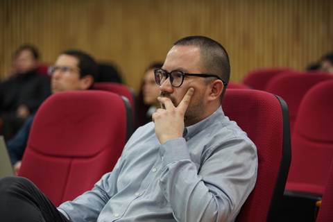 Un hombre en un auditorio, pensativo mientras escucha una charla.