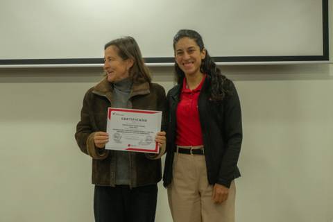 Dos mujeres posan felices mostrando un certificado en un evento.