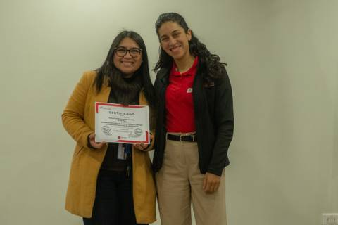 Dos mujeres posando felices con un certificado en un entorno neutral.