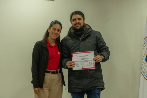 Dos personas sonríen mientras sostienen un certificado en un evento de entrega.
