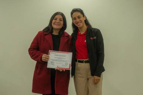 Dos mujeres posando felices con un certificado en mano.